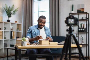 African american blogger unboxing new smartphone and recording video on camera. Young guy sharing with subscribers his feedback about modern gadget.