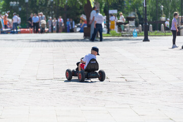 A boy rides an electric car on the square in the park.