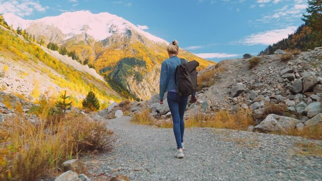 A young beautiful slender woman alone in the mountains. She walks in a denim jacket and jeans and enjoys the beautiful scenery of the highlands in autumn. Hiking. Georgia. A lonely journey.
