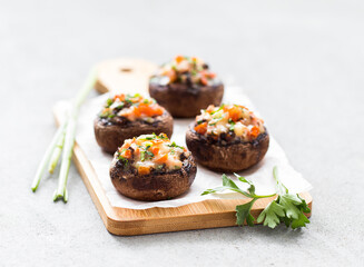 Stuffed champignons with ham, cheese, tomatoes and parsley on a wooden board on a light gray background
