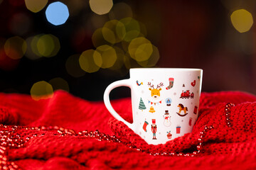 White cup with a New Year's pattern on a red knitted blanket on a dark background on the side, Christmas still life
