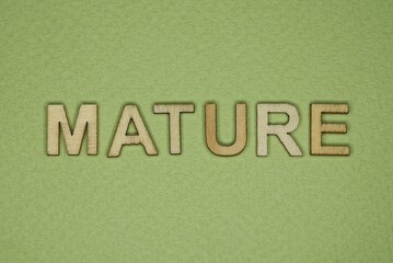 gray word mature from small wooden letters on a green table