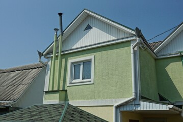 green concrete attic of a private house with a white window and chimneys against a blue sky