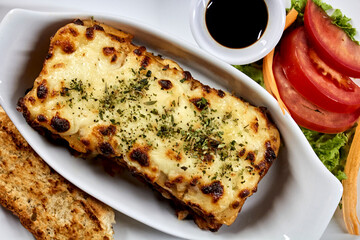 lasagna on white plate with bread and salad