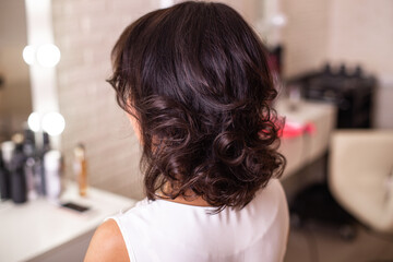 Female back with short curly brunette hair in hairdressing salon