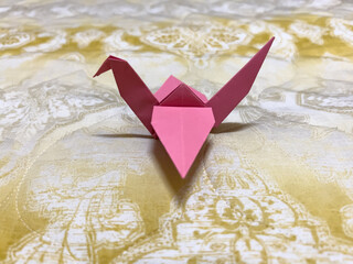 pink origami crane on a gold mat
