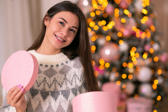 Happy, cute woman received a gift for the new year holiday. Girl smiling with braces on her teeth, celebrating merry christmas, holding a gift in her hands