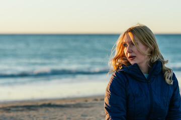 Blonde woman with relaxed expression on a beach during sunset