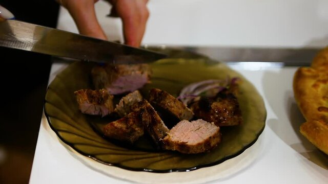 The girl cuts meat on the festive table, cooking food in the kitchen in the apartment.