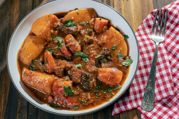 Aerial view of a plate with homemade meat, potato and vegetable stew on a wooden table