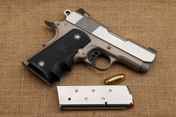 .45 automatic handgun with bullet magazine on burlap background , Classic gun