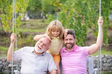 Grandfather with son and grandson on a swing in spring garden outdoors. Active pring leisure for...