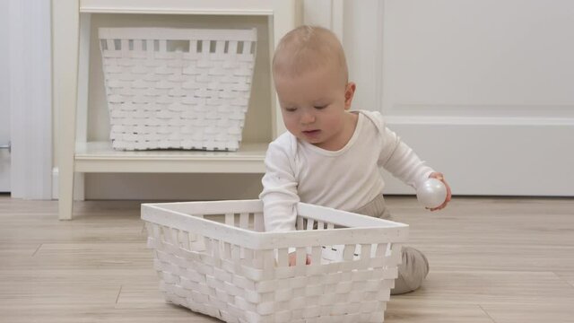 Baby sitting on the floor playing with plastic balls from toy storage basket, cute 9 month old baby boy having fun taking out ball from basket at hom. High quality 4k footage