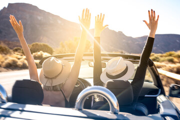 Dreams come true! Two happy young girls driving cabrio car during vacation road trip in mountains,...