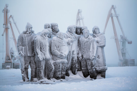 Anadyr, Chukotka, Russia - November 26, 2013. Monument to the revolutionaries on the banks of the Anadyr estuary. A view of the sculptures covered with frost and snow and the cranes of the seaport.