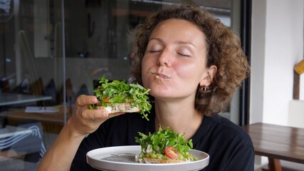 Lady eating with hands big healthy avocado toast with green salad and cherry tomatoes on white plate 