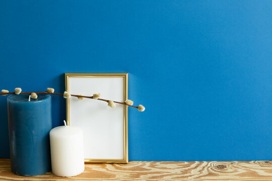 Gold Picture Frame And Candle On Wooden Table. Blue Wall Background. Copy Space