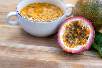 Half of the passion fruit (maracuya) with fruit pulp and passion fruit seeds in a bowl on  wooden table, Passion fruit, a fruit that is sour and high in vitamins.