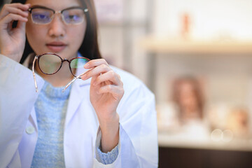 Professional optician holding and checking glasses in optical store, vision and eye care concept, selective focus