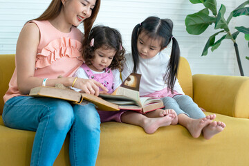 Lovely family, pretty mother and two daughters reading a book on couch, little girls interest at book