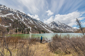 Obraz premium Hiker in blue jacket standing beside a isolated, wilderness lake in northern Canada during spring time, May. 