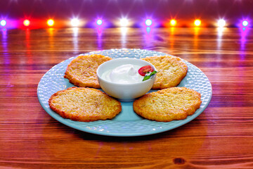Potato pancakes or latkes on a blue plate of rustic wooden surface with sour cream