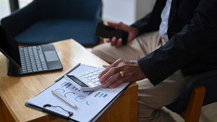 Cropped shot senior businessman holding mobile phone and using calculator in office.