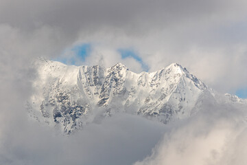 Snowy covered mountain top on winter with misty, cloud covered snow, high altitude peak. Landscape, stunning nature background. 