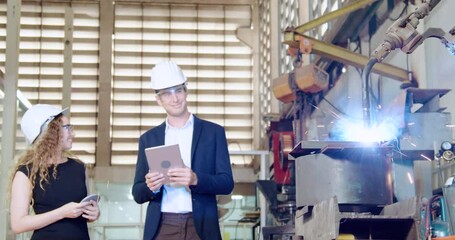 Professional engineer wearing safety glass and hard hat visit factory closeup monitor robot arm welding machine spark anamorphic flare equipment moving near metal table 
