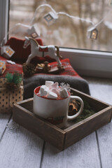A mug with marshmallows is on the table in a wooden box, next to a sweater and a toy horse.