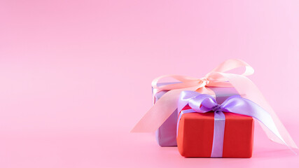 Gift wrapped in red wrapping paper and ribbon on a pink background close-up.