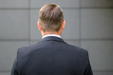 Rear view of a businessman in a suit facing a grey wall