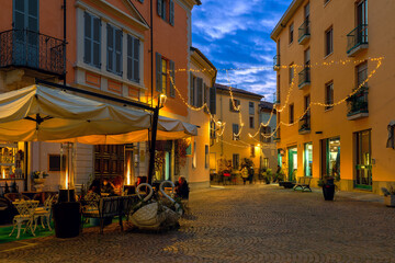 Outdoor restaurant on town square illuminated with Christmas lights in Alba, Italy.