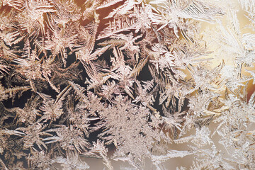 Winter background. Brown with yellow tinted wallpaper. Drawing of crystals of ice and frost on the window glass. Frozen surface. Abstract backdrop