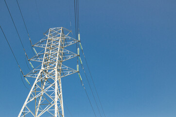 High Voltage Overhead power line standing against blue sky day.