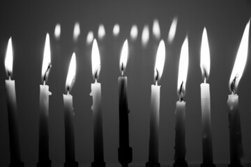 Black and white of a full menorah on the last night of Hanukkah. All nine candles are lit in a dark room and reflecting in the background. © ShakedN