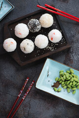 Black wooden serving tray with onigiri or japanese rice balls, above view over dark-grey stone background, vertical shot
