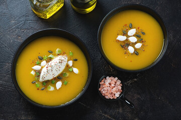 Black bowls with pumpkin cream-soup over dark brown stone background, top view, horizontal shot