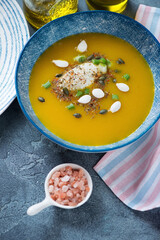 Pumpkin cream-soup with addition of cheese, pumpkin seeds and scallions served in a blue bowl, vertical shot, middle close-up