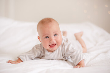 the baby is lying at home on the bed smiling