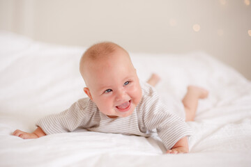 the baby is lying at home on the bed smiling