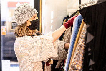 A customer with a protective mask looking at new collection clothes on a hanger, second-hand and sustainable clothing store, coronavirus, covid-19