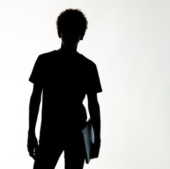 silhouette a teenage boy with afro hair holding a laptop with his left hand, against the light
