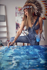 A young sexy female artist with a war bonnet is relaxed when she is painting in her studio. Art, painting, studio