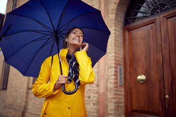 A young cheerful woman is listening to the music while walking the city on a rainy day. Walk, rain,...