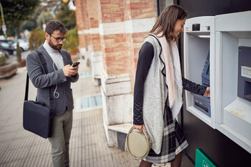A young attractive woman is using ATM machine on the street. Walk, ATM, city