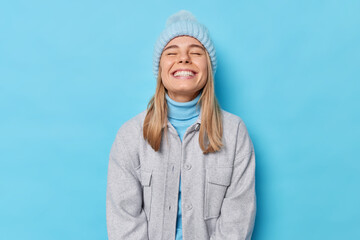 Beautiful sincere woman keeps eyes closed smiles toothily enjoys life wears knitted hat turtleneck...