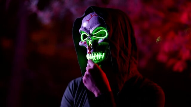 suit for Halloween, mask with glowing skull, green lights in darkness on street in night