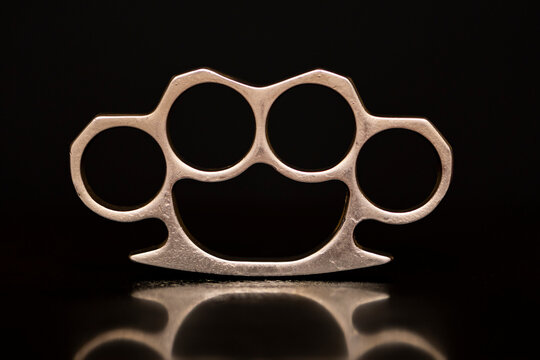 Steel brass knuckles on a black background with reflections. Concept: hooligan fight, fighting without rules, street banditry, injuries.