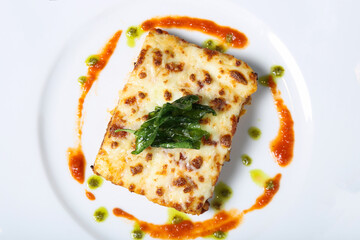 A slice of lasagne with sauce on a white plate